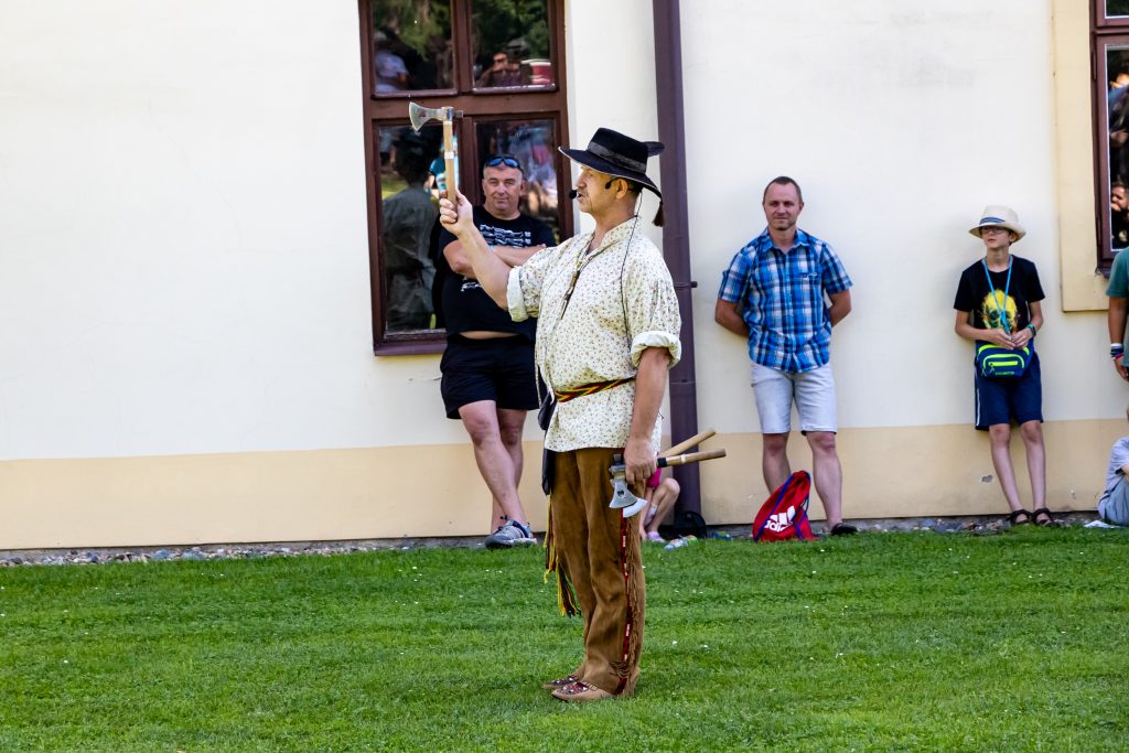 Kostýmovaný muž v klobouku vystupuje před diváky na nádvoří historické budovy.