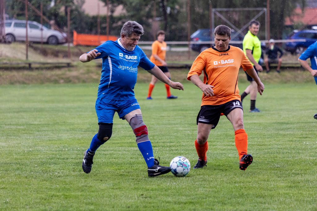 Fotbalista v modrém dresu zpracovává míč před soupeřem v oranžovém.
