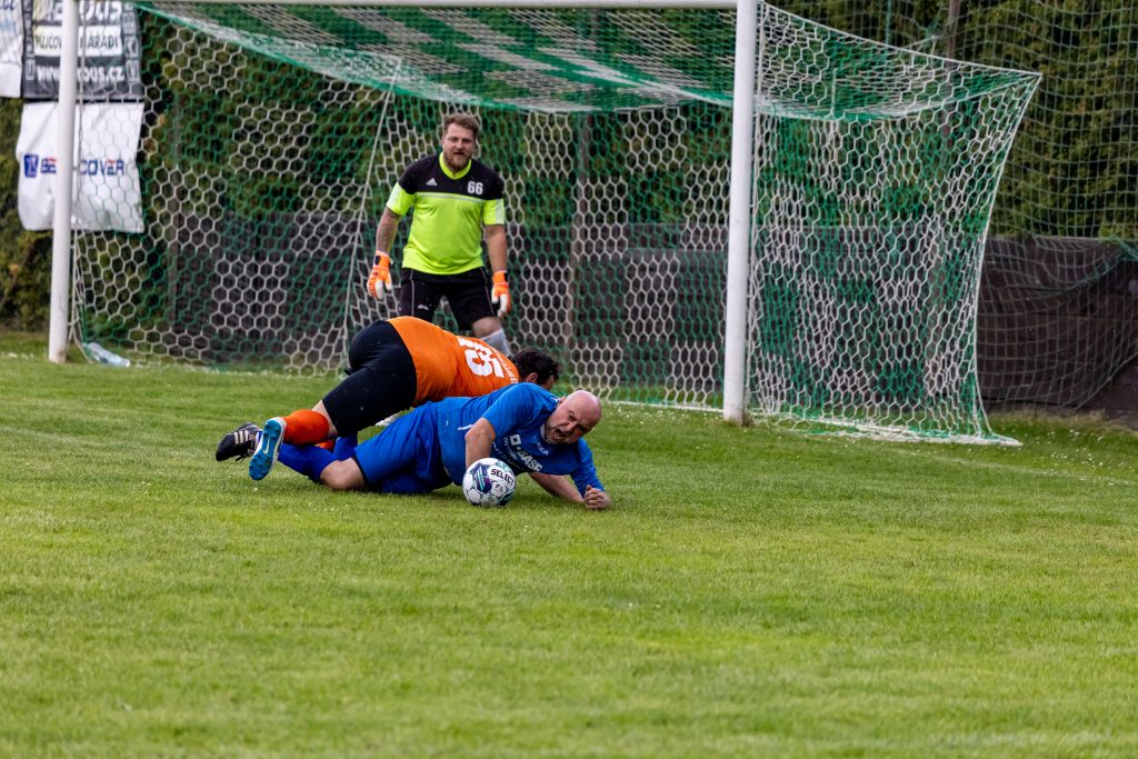 Dva fotbalisté padají v souboji o míč před brankou.