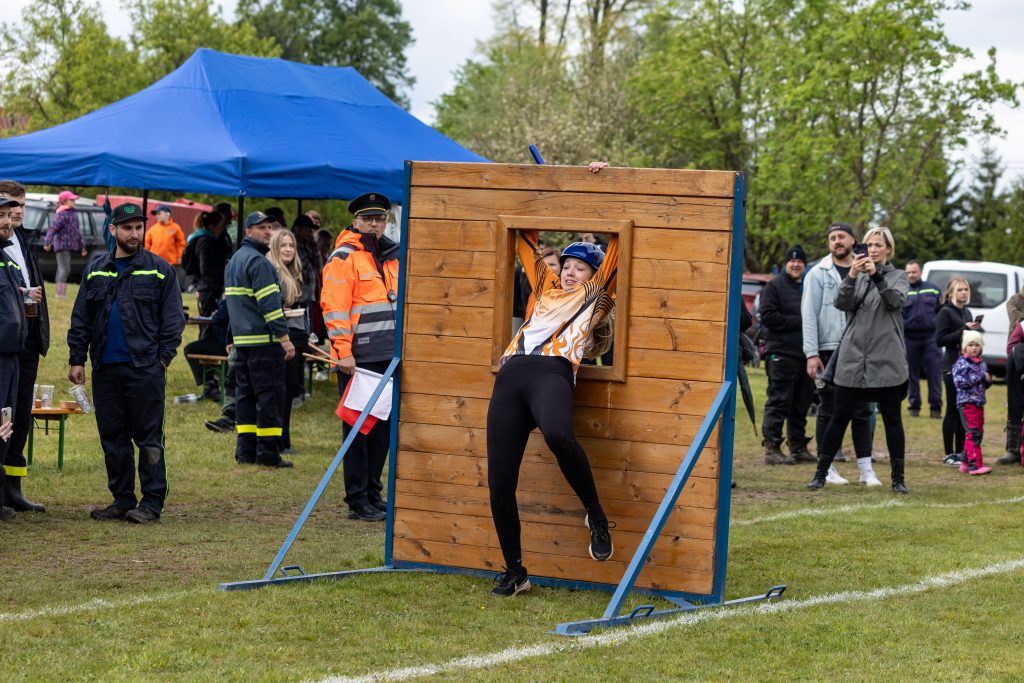 Závodnice prolézá oknem dřevěné překážky před diváky.
