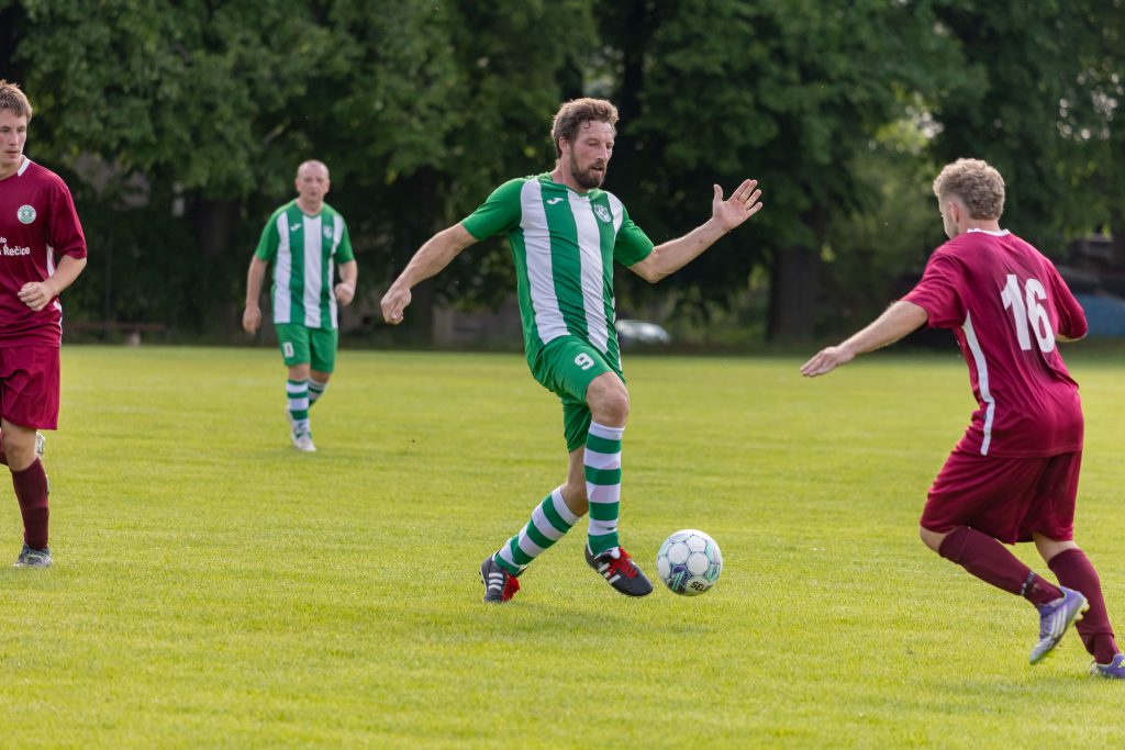 Fotbalista v zelenobílém dresu kličkuje proti obránci ve vínovém.