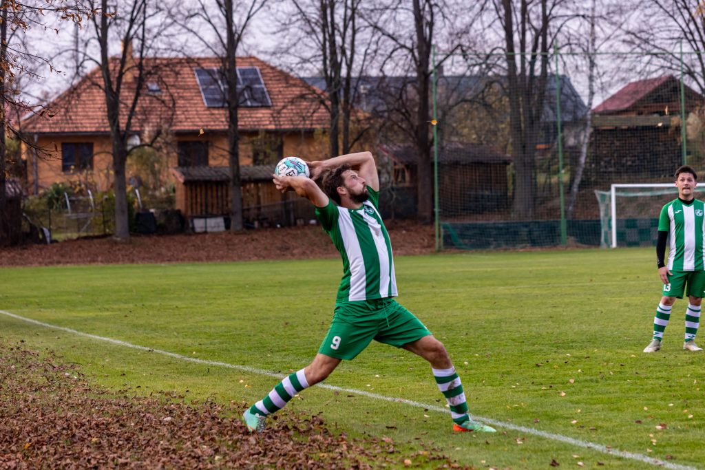 Fotbalista v zelenobílém dresu vhazuje míč ze zámezí.