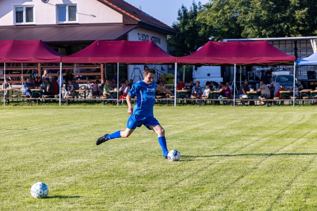 Fotbalista v modrém dresu se rozbíhá k volnému míči u postranní čáry.