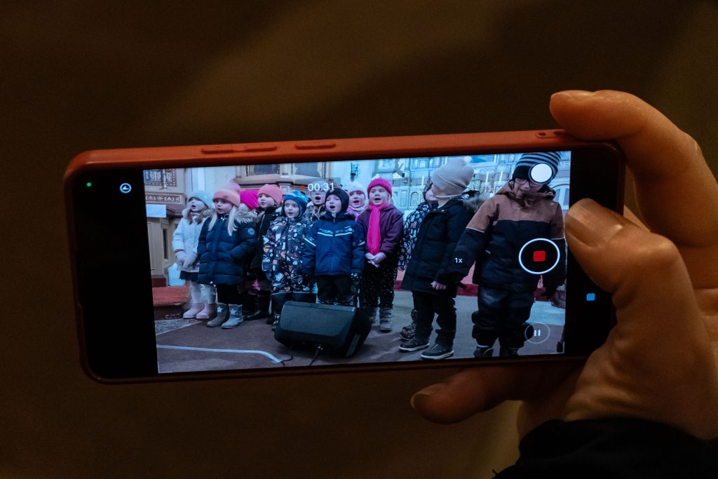 Mobilní telefon v ruce natáčí vystoupení dětského pěveckého sboru.
