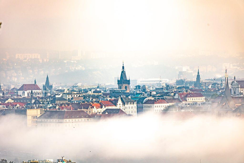 Pražské věže a střechy vystupující z vrstvy ranní mlhy.