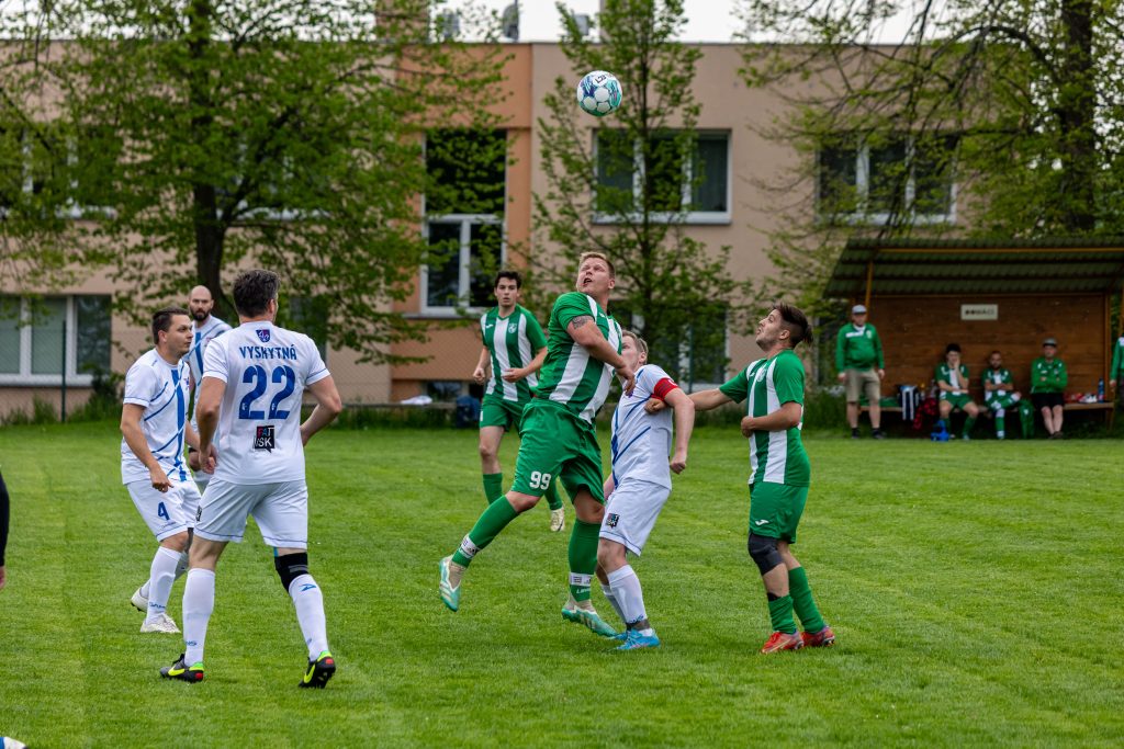 Fotbalisté v zeleném a bílém sledují míč při hlavičkovém souboji.
