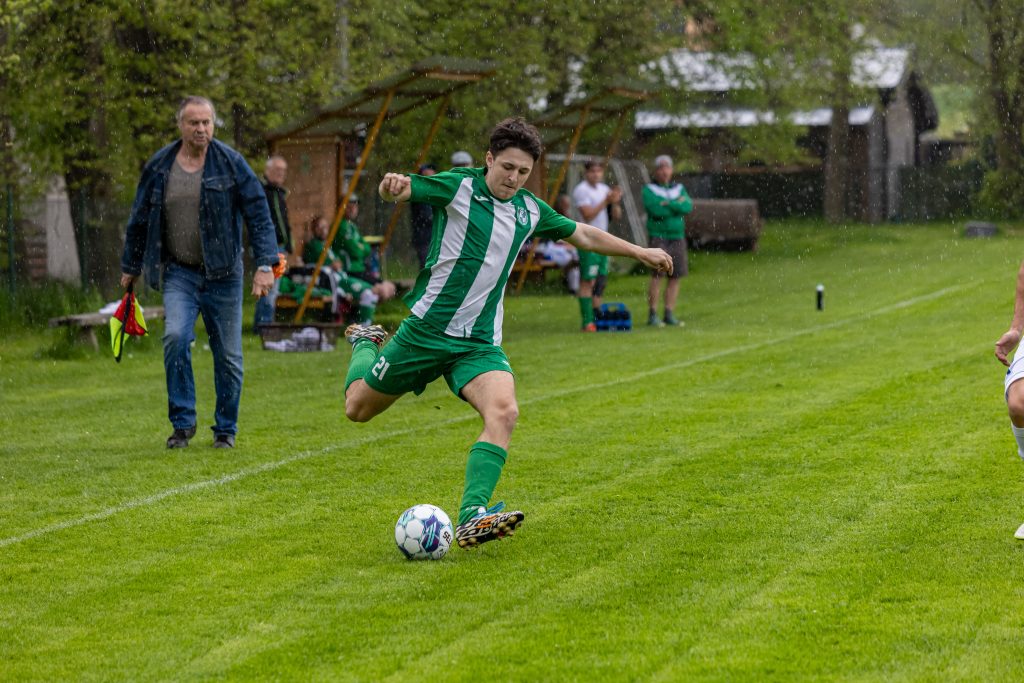 Fotbalista v zelenobílém dresu napřahuje ke střele pravou nohou.