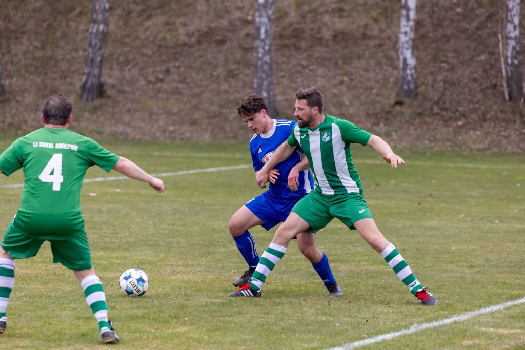 Tři fotbalisté bojují o míč u postranní čáry.