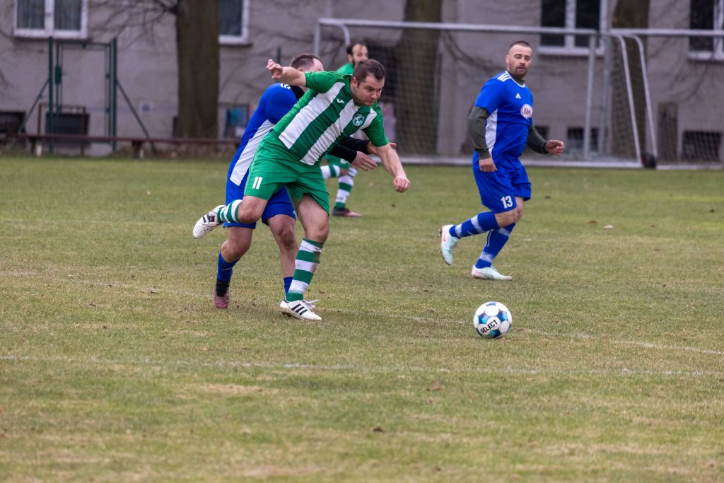 Fotbalista v zelenobílém dresu uniká s míčem mezi hráči v modrém.