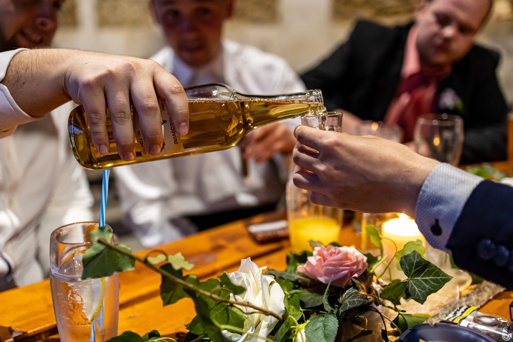 Ruka nalévá světlé pivo z lahve do sklenice u slavnostně prostřeného stolu.